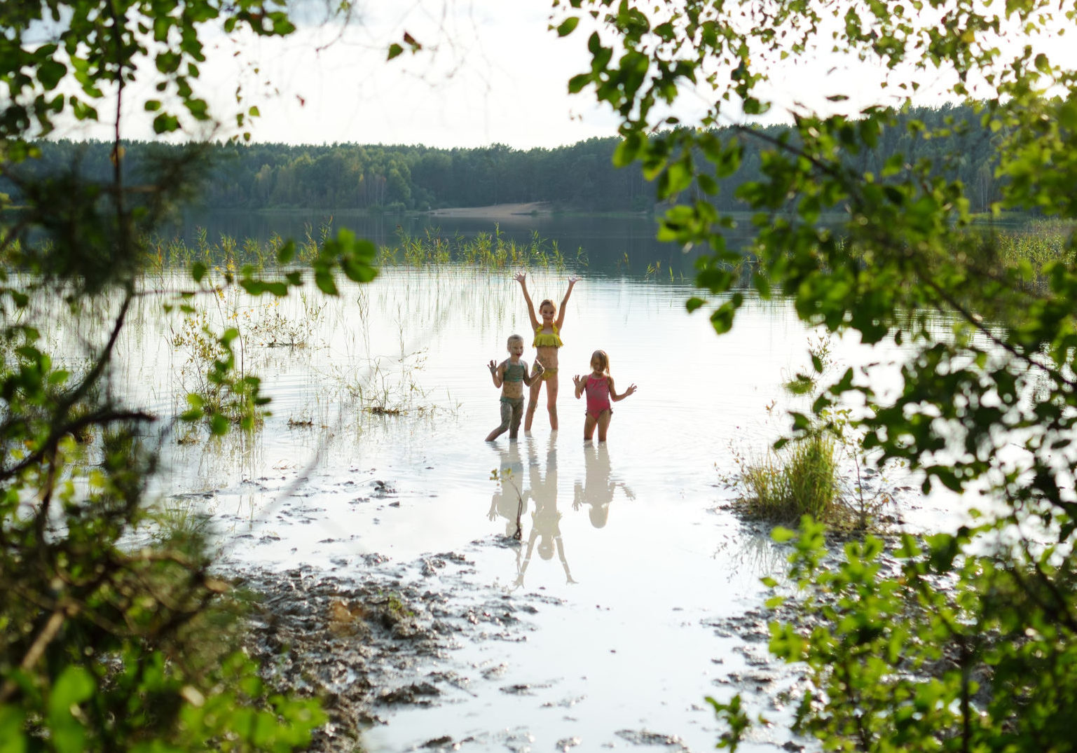 Three young sisters taking healing mud baths on lake Gela near Vilnius, Lithuania. Children having fun with mud. Kids playing with medicinal clay.